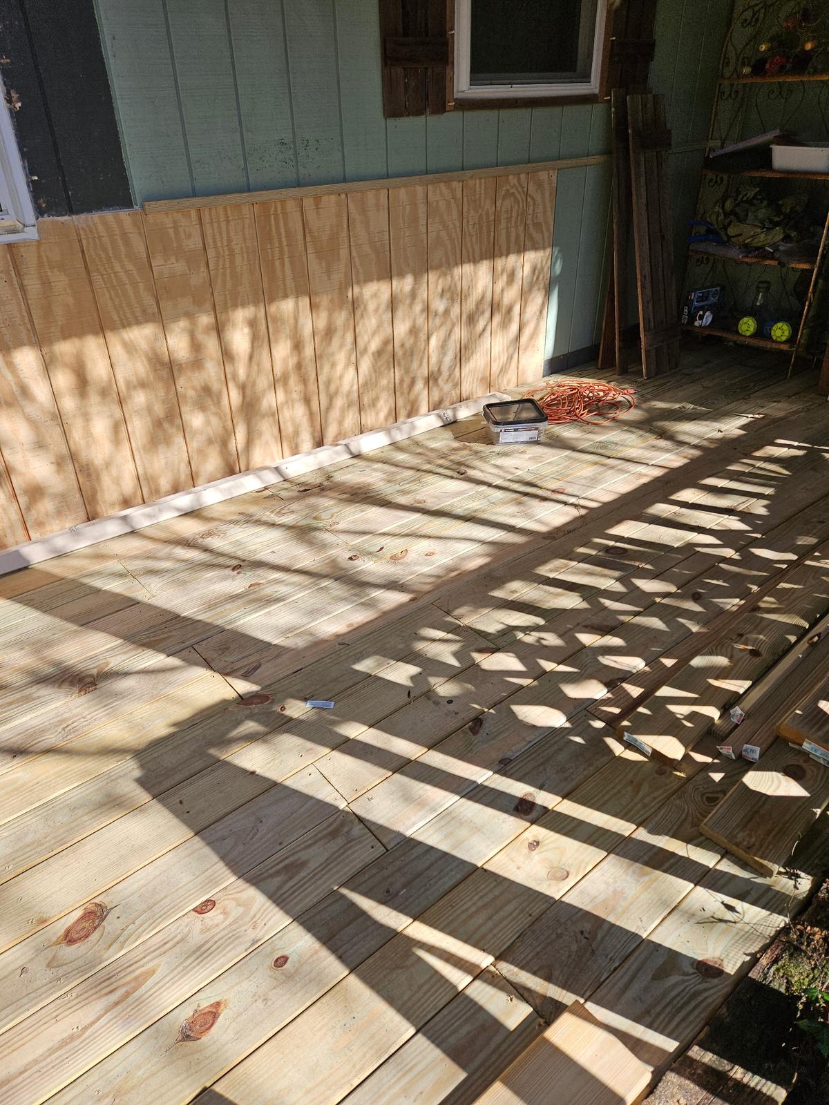 Screened porch mid-rebuild — new deck boards and plywood wainscot going in